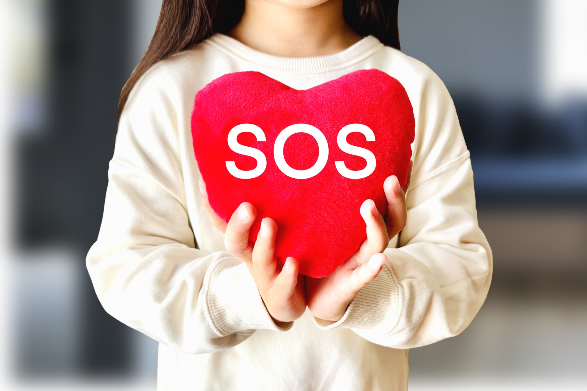 SOSと書かれたハート形のぬいぐるみを差し出す子ども